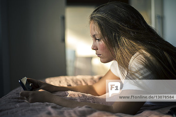 Teenager-Mädchen benutzt Mobiltelefon  während sie zu Hause im Bett liegt
