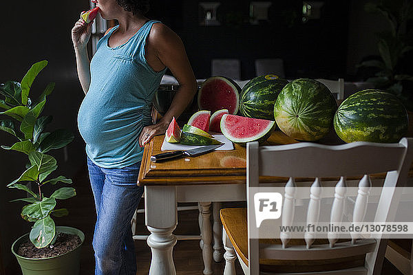 Mittelsektion einer schwangeren Frau  die am Tisch steht und Wassermelone isst