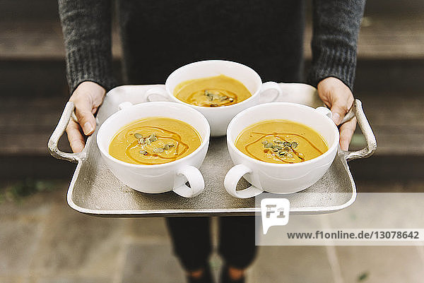 Midsection of woman carrying pumpkin soup in bowls on serving tray