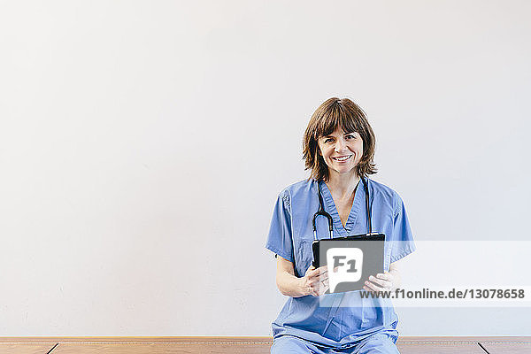 Porträt einer Ärztin  die einen Tablet-Computer hält  während sie auf einer Bank vor weißem Hintergrund sitzt