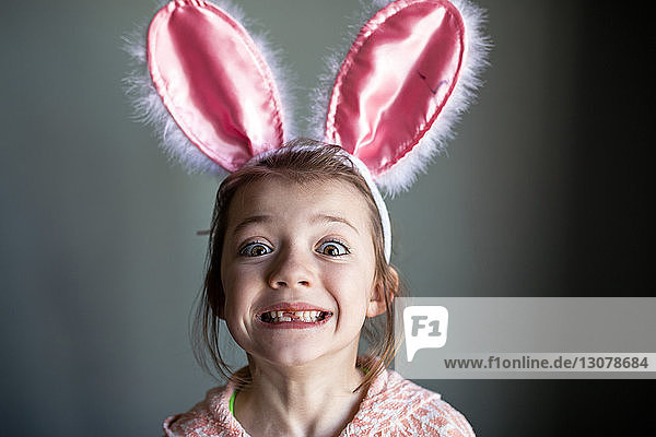 Porträt eines verspielten Mädchens  das ein Stirnband mit Kaninchenohren trägt und zu Hause eine Zahnlücke zeigt