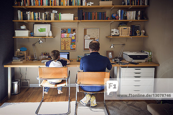 Rückansicht von Vater und Sohn am Laptop zu Hause