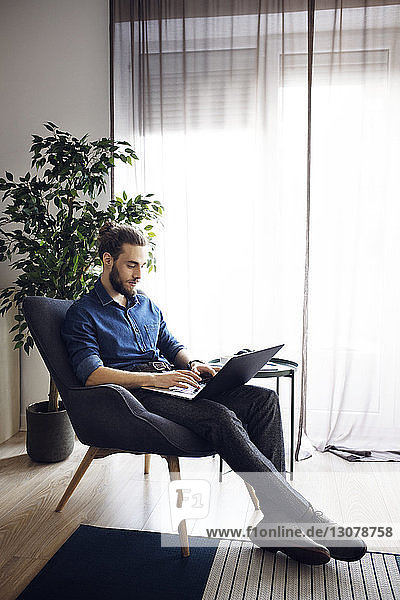 Man using laptop computer while sitting on chair at home