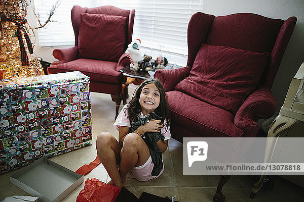Hochwinkelporträt eines glücklichen Mädchens mit Weihnachtsgeschenk  das zu Hause auf dem Boden sitzt
