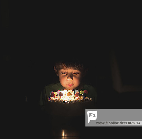 Junge bläst Geburtstagskerzen auf Torte in der Dunkelkammer