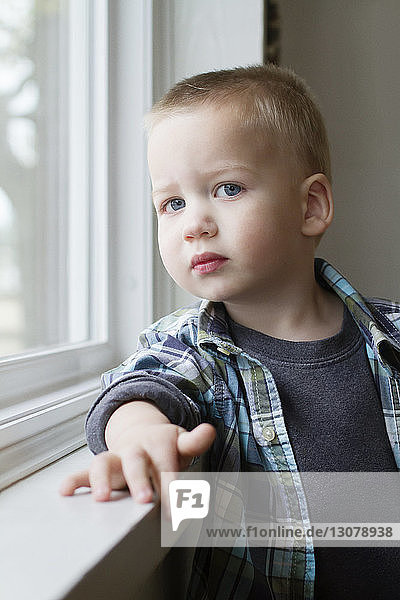 Porträt eines süßen Jungen  der zu Hause am Fenster steht