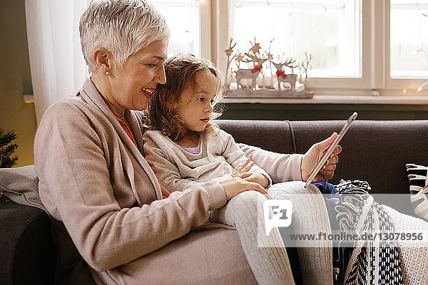 Großmutter mit Enkelin benutzt Tablet-Computer  während sie sich zu Hause auf dem Sofa entspannen