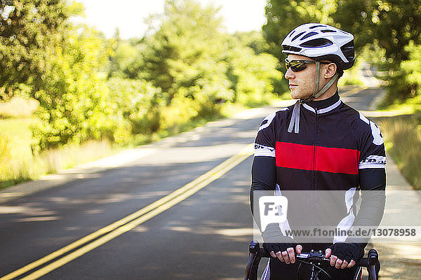 Athlete looking away while standing with bicycle on road