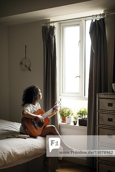 Frau schaut weg  während sie zu Hause Gitarre spielt