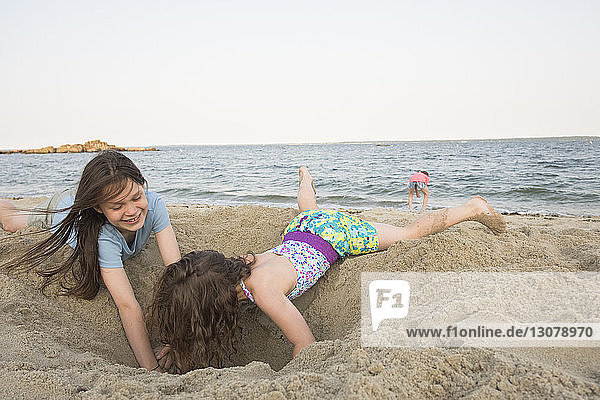 Sisters playing with sand at beach against clear sky