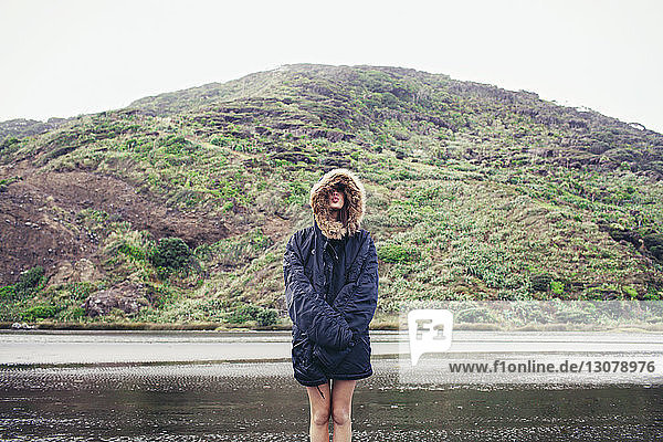 Frau trägt Jacke und steht am nassen Strand gegen Berg