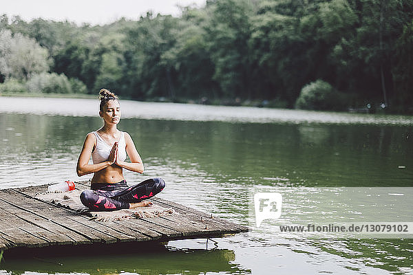 Frau meditiert  während sie am Pier über einem See im Wald sitzt