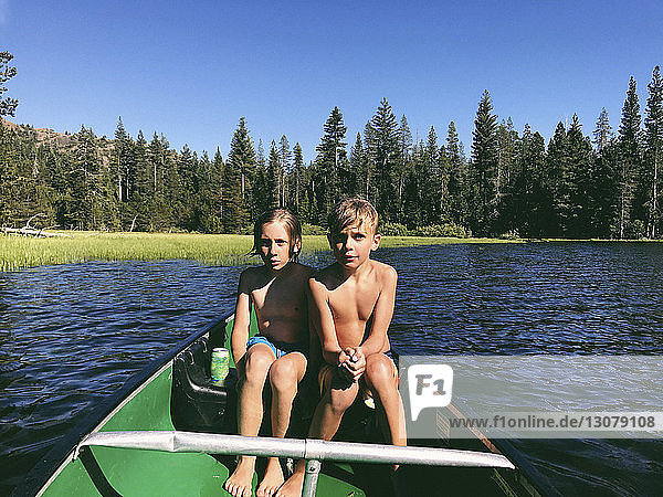 Shirtless brothers sitting in boat on Rucker Lake during sunny day at forest