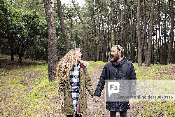 Fröhliches Paar hält im Wald Händchen und steht