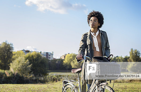 Nachdenkliche Frau mit Fahrrad steht auf dem Feld vor klarem Himmel