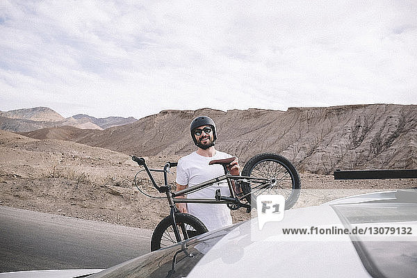 Porträt eines Mannes  der ein Fahrrad auf ein Auto lädt  vor Bergen und bewölktem Himmel
