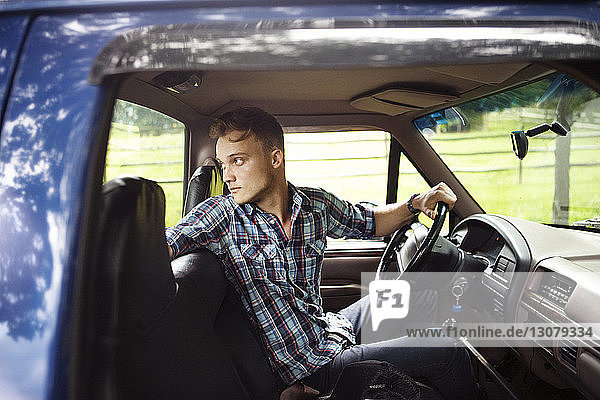 Man looking over shoulder while driving pick-up truck seen through window
