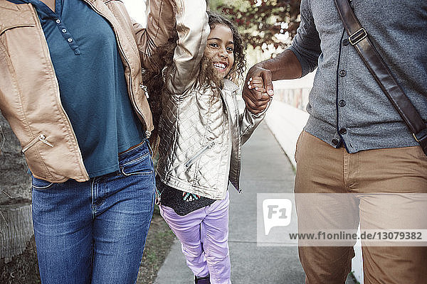 Glückliche Tochter mit Eltern  die auf dem Bürgersteig gehen