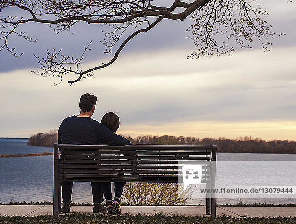 Vater und Sohn schauen auf die Aussicht  während sie auf einer Parkbank am See sitzen