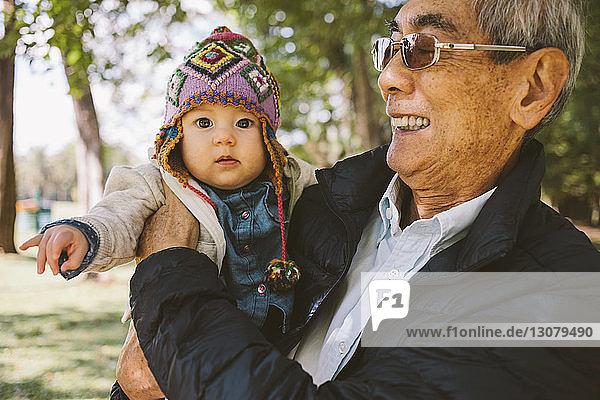 Portrait of granddaughter being carried by grandfather at park