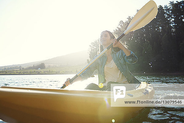 Smiling woman looking away while kayaking on lake against sky during sunny day