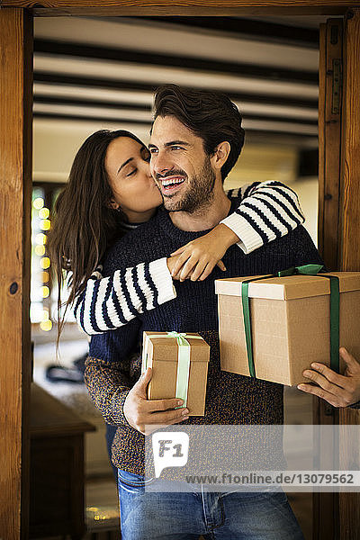 Frau küsst ihren Freund mit Geschenkkartons an der Tür