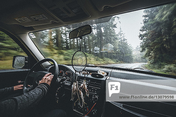Cropped hands of man driving car on road amidst forest
