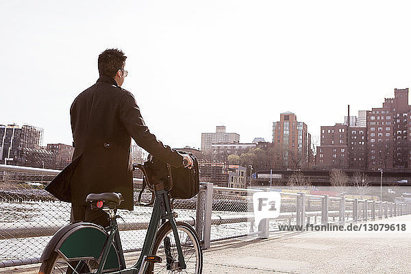 Rückansicht eines Geschäftsmannes zu Fuß mit dem Fahrrad auf einem Fußweg in der Stadt