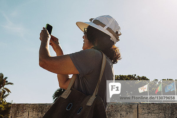 Niedrigwinkelansicht einer älteren Frau  die an einem sonnigen Tag durch ein Smartphone fotografiert