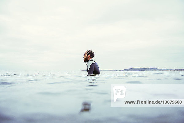 Seitenansicht eines männlichen Surfer im Meer vor bewölktem Himmel