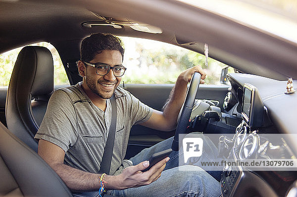 Portrait of smiling man with mobile phone traveling in car