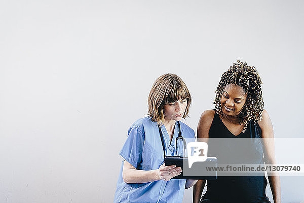 Doctor showing pregnant woman ultrasound on tablet computer while sitting against white background