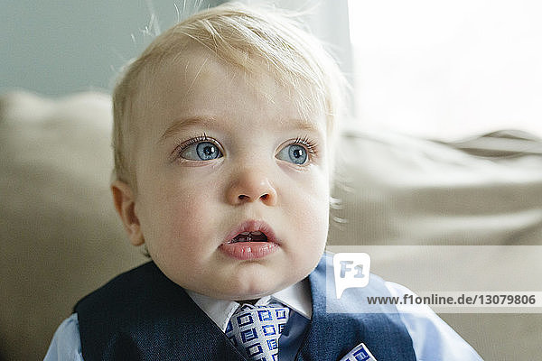 Nahaufnahme eines nachdenklichen kleinen Jungen im Anzug  der während der Osterfeierlichkeiten zu Hause auf dem Sofa wegschaut