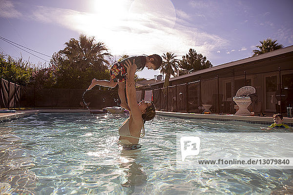 Glückliche Mutter hebt Jungen im Schwimmbad eines Touristenortes
