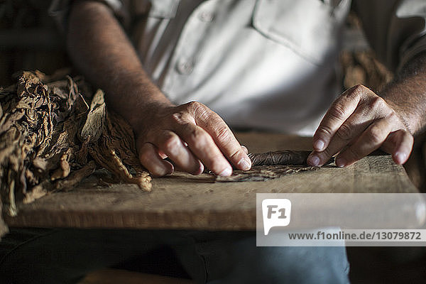 Midsection of man rolling dry leaves on table at workshop