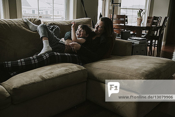 Glückliche Mutter spielt mit ihrem Sohn  während sie zu Hause auf dem Sofa liegt