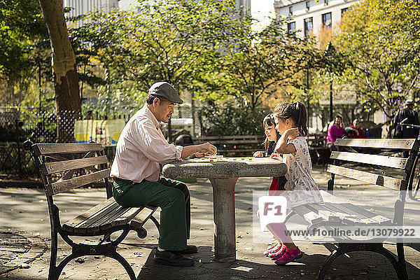 Seitenansicht von Großvater und Enkelinnen beim Spiel auf einer Parkbank sitzend