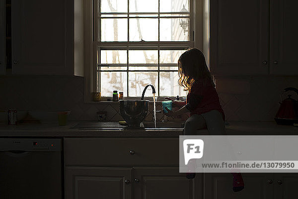 Mädchen spielt mit Wasser an der Küchenspüle