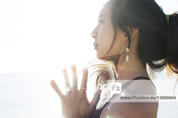 Side view of thoughtful sporty woman with hands clasped against clear sky on sunny day