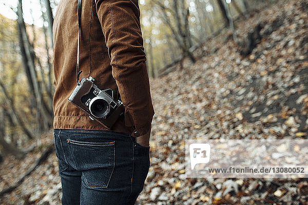 Midsection of man with camera standing in forest during autumn
