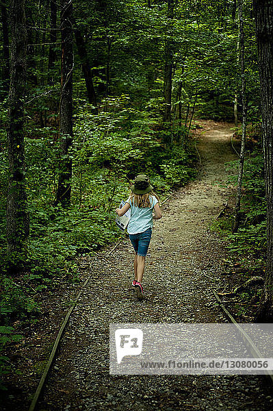 Rear view of girl running on footpath amidst trees at forest