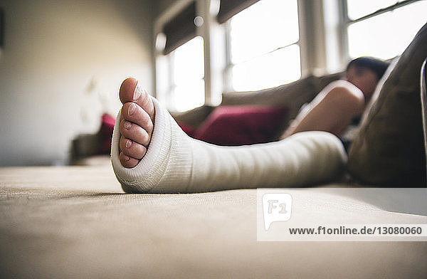 Close-up of boy with fractured leg sitting on sofa at home