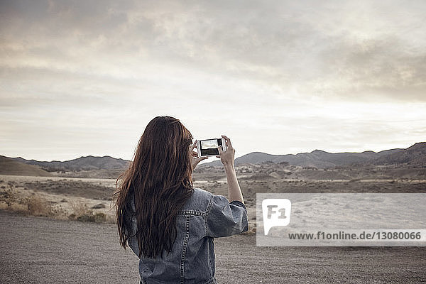 Rückansicht einer Frau  die den Berg fotografiert  während sie auf dem Feld steht