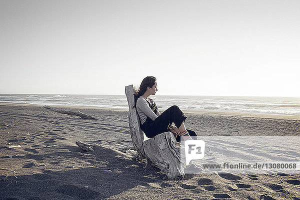 Thoughtful woman relaxing on wood at beach