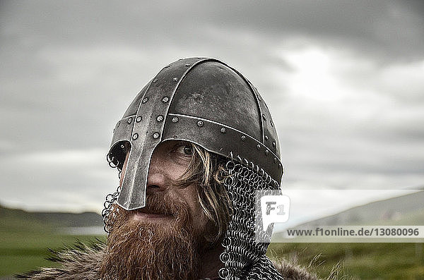 Nahaufnahme eines Kriegers mit traditionellem Helm  der auf einem Grasfeld vor bewölktem Himmel steht