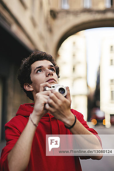 Teenage boy looking up while holding camera in city