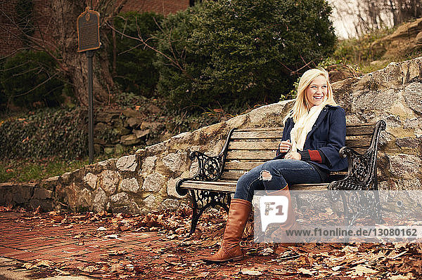 Smiling woman sitting on bench at park during winter