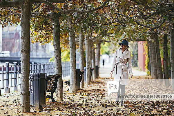 Frau im Mantel geht im Herbst auf einem Fußweg im Park