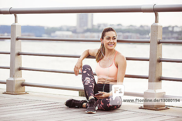 Glückliche Frau in Sportkleidung schaut weg  während sie auf der Brücke Musik hört
