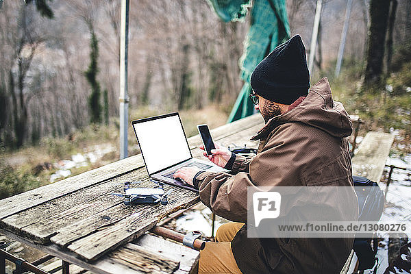 Seitenansicht eines männlichen Wanderers mit Mobiltelefon und Laptop-Computer auf einem Tisch im Wald